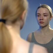 woman looking at herself in mirror with self-loathing